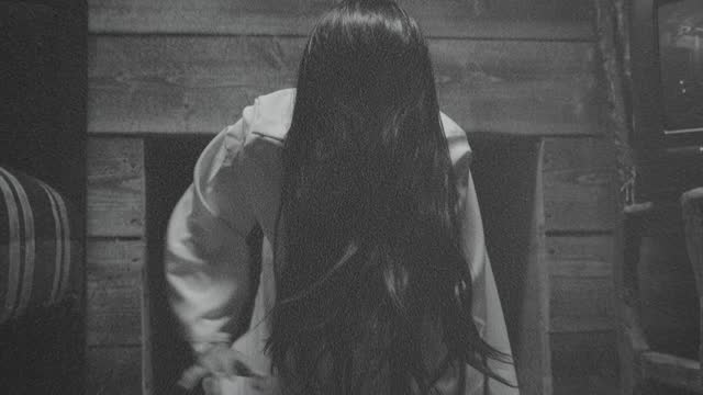 Scary Ghost Woman Crawling or Walking In Horror Halloween Scene . Droning television inside dark empty room . Little girl in white sundress . Girl with long black hair.