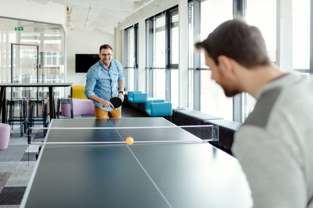 Colleagues Playing Ping Pong Table Tennis Happy young friends playing ping pong table tennis at office break out area. Concept of healthy sport and genuine emotions. Lifestyle, rest concepts ping pong tournament stock pictures, royalty-free photos & images