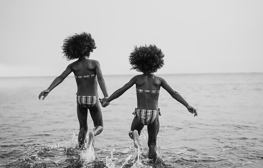 Happy african sister twins running on the beach together - Black and white editing