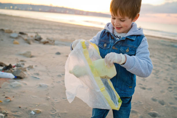 istock Child volunteer cleans a beach by gathering discarded plastic waste. Environmental pollution and ecological problems concept. 1474788346