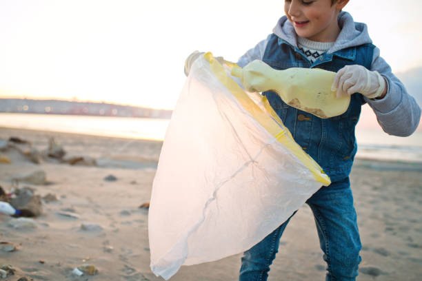 istock Child volunteer cleans a beach by gathering discarded plastic waste. Environmental pollution and ecological problems concept. 1474788357