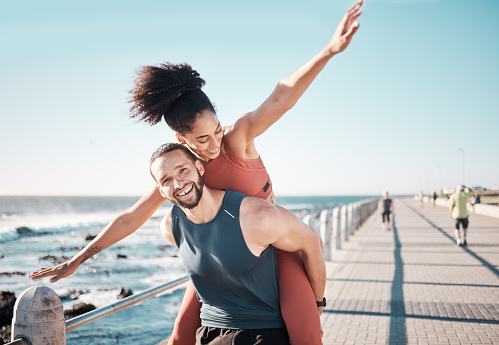 Beach, fitness and couple piggyback in summer enjoying holiday, vacation and quality time on weekend. Love, dating and black man and woman relax after running, exercise workout and training by ocean