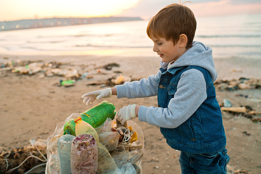 Little boy picking up garbage near the sea