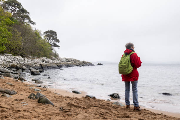 Wide shot rear view of a senior couple woman standing looking out at the ocean while on a hiking staycation in Dumfries and Galloway, Scotland.
