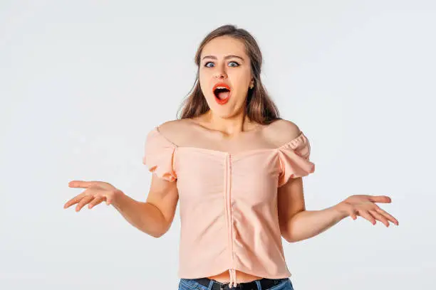 Excited and wonder people. Surprised young woman shouting with raising hands up, shrugs. Excited girl looks amazed, stands against neutral studio background