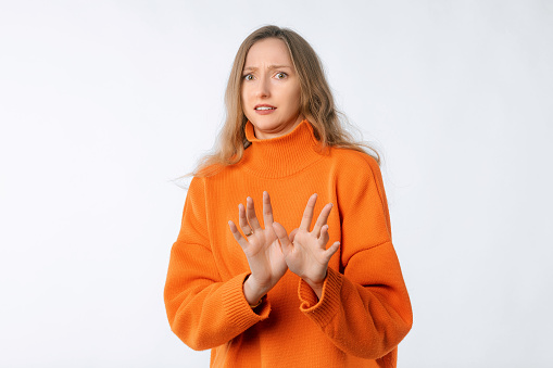 Portrait of young woman deny something, shakes hands and say no, rejects offer, looks insulted, express disapproval, wearing soft orange sweater, standing over neutral background