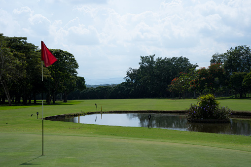 Red golf flag in a golf hole near a pond.