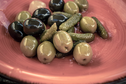 Close-up shot of mix of black and green olives with pickle in an orange bowl.