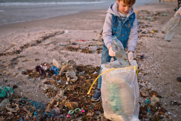 istock Child volunteer cleans a beach by gathering discarded plastic waste. Environmental pollution and ecological problems concept. 1474789880