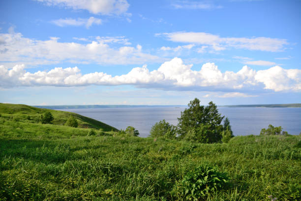 istock A grassy hill with green tree, blue sky and white clouds on horizon with river 1474792215