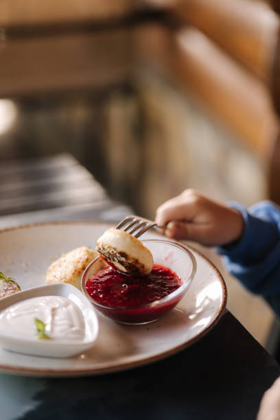 istock Children's hand pricks on a fork curd fritters. Cheesecake, fresh jam, sour cream and mint. 1474794199