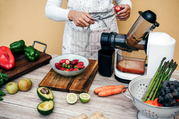 istock Young woman preparing organic juice with cold pressed extractor machine - Main focus on right hand holding strawberry 1474794242