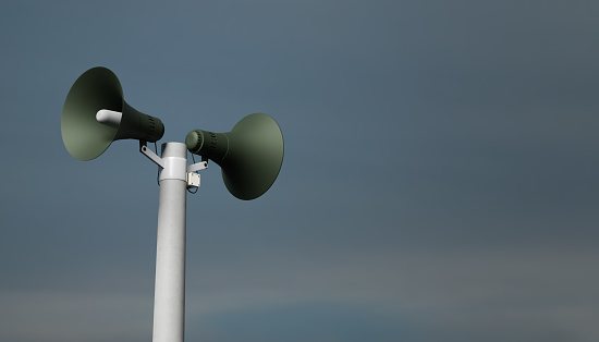 Megáfonos de notificación de megafonía en una publicación, representación 3D. Altavoces de notificación al aire libre para anuncio o alerta de ataque aéreo, fondo del cielo photo