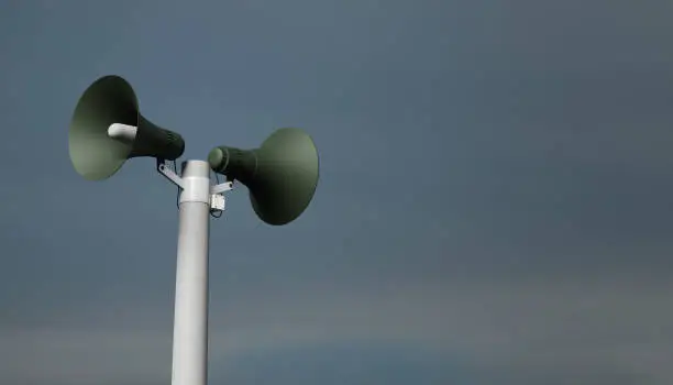 Photo of public address notification megaphones on a post, 3d rendering. Outdoor notification loudspeakers for announcement or air raid alert, sky background