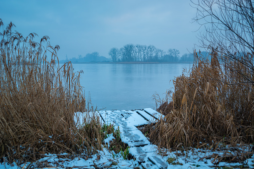 A snow-covered wooden platform in the reeds and a frozen misty lake, Stankow, Poland