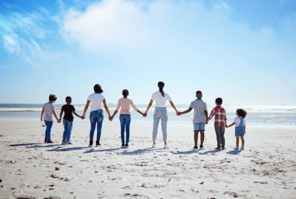 apoio, costas e grande família de mãos dadas na praia, caminhadas de verão e viagens de férias na natureza de portugal. esperança, amor e mulheres com carinho por crianças adotadas em férias no oceano - adoption early teens teenager family - fotografias e filmes do acervo