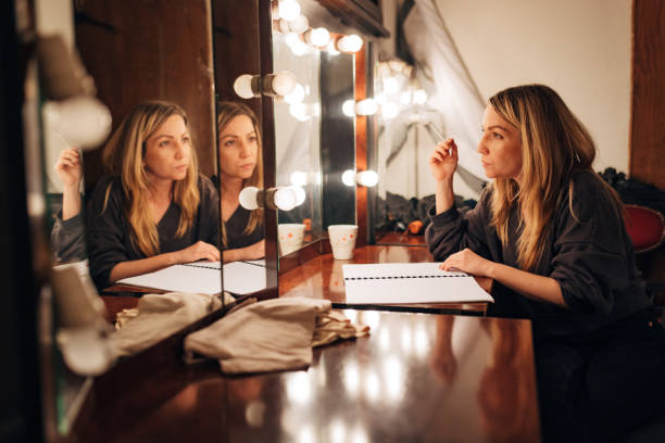 The actress in the dressing room rehearses the scene sitting in front of the mirror before the performance A theater actress sits in the theater's make-up room in front of a mirror and rehearses the text of the play theatre mirror stock pictures, royalty-free photos & images