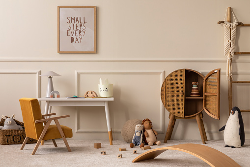 Creative composition of children room interior with mock up poster frame, white desk, yellow armchair, plush toys, pouf, rattan sideboard, gray lamp and personal accessories. Home decor. Template.