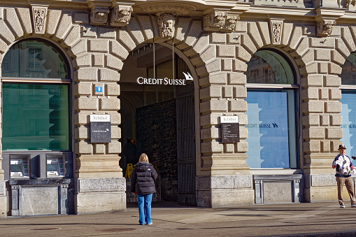 Woman at entrance of headquarters of Credit Suisse bank with people at day after rescue deal on a sunny later winter morning. Photo taken March 20th, 2023, Zurich, Switzerland.