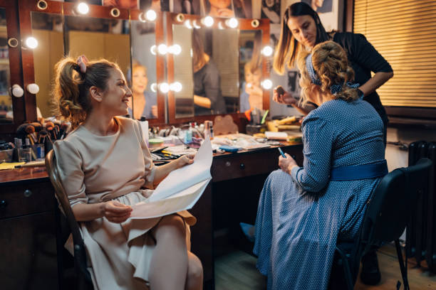 istock Cheerful actress holds a script in her hands as she watches a make-up artist apply make-up to her senior colleague 1474801097