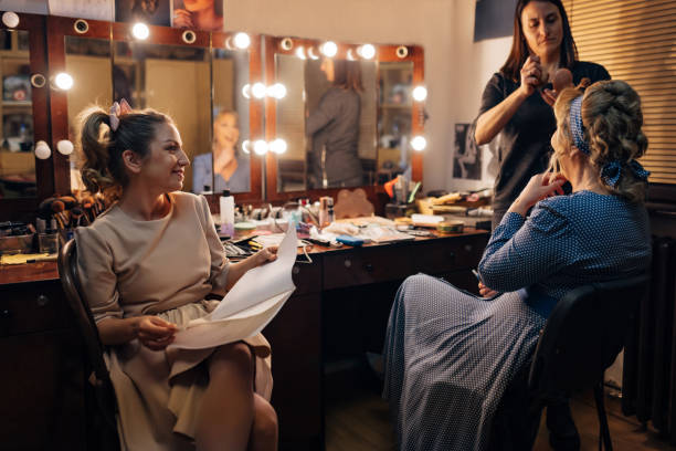 istock Cheerful actress holds a script in her hands as she watches a professional make-up artist apply make-up to her senior colleague 1474801129