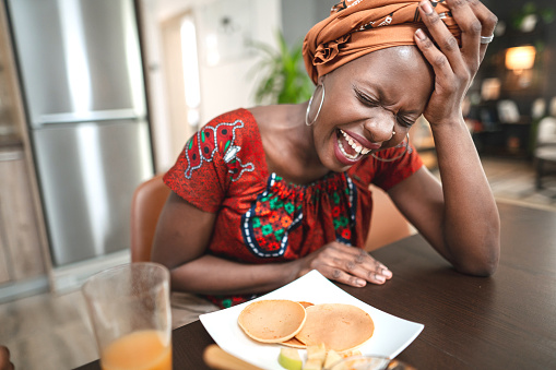 Black woman laughing while eating breakfast in the kitchen