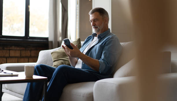 istock Happy smiling senior man using smartphone device while sitting on sofa at home 1474802610