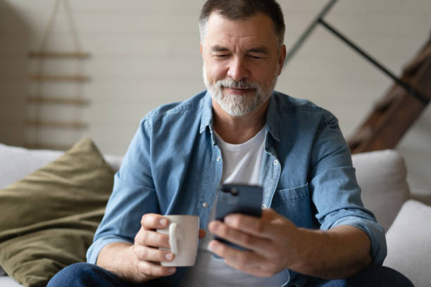 istock Happy smiling senior man using smartphone device while sitting on sofa at home 1474802622