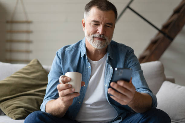 istock Happy smiling senior man using smartphone device while sitting on sofa at home 1474802629