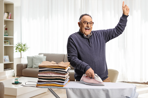 Cheerful mature man ironing clothes and dancing at home