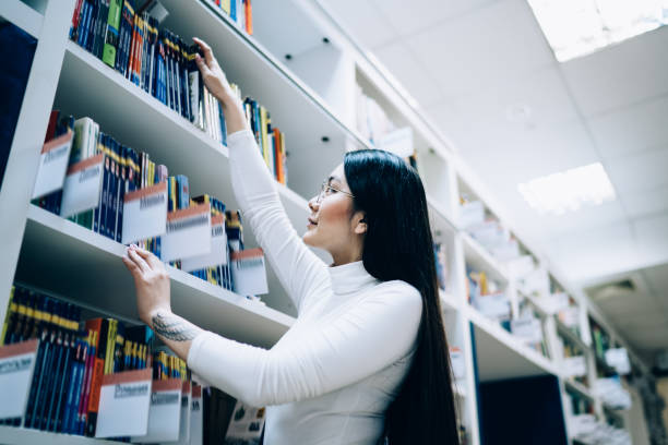 istock Young female choosing book in library 1474804511