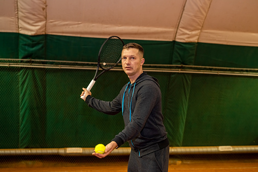professional tennis player is hitting tennis on an indoor tennis court from early morning. Dressed in sports clothes. hitting the ball with a racket