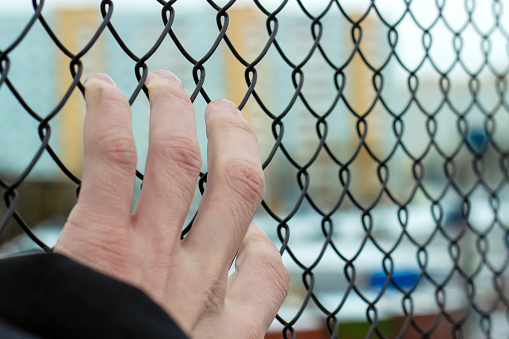 hand holding on to a mesh fence, blurred background