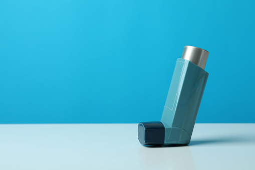 Asthma inhaler on white table against blue background