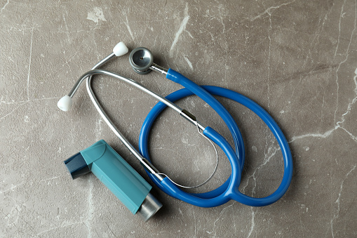 Asthma inhaler and stethoscope on gray textured table