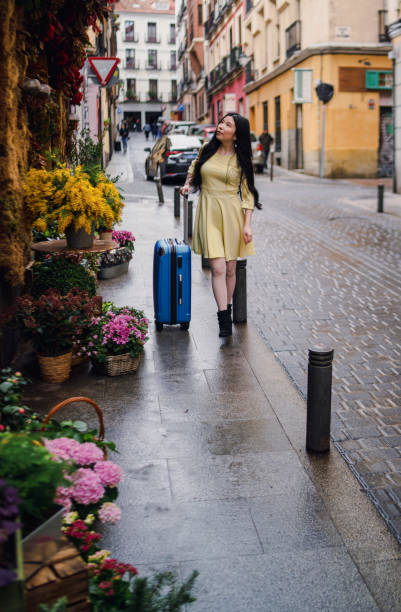 A tourist girl with her suitcase enjoying a flower shop in the street. stock photo