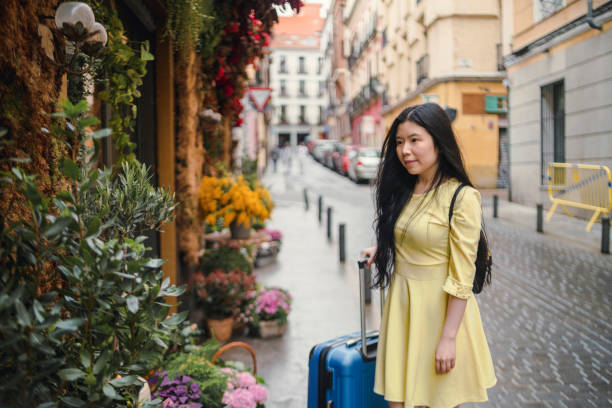 A tourist girl with her suitcase enjoying a flower shop in the street. stock photo