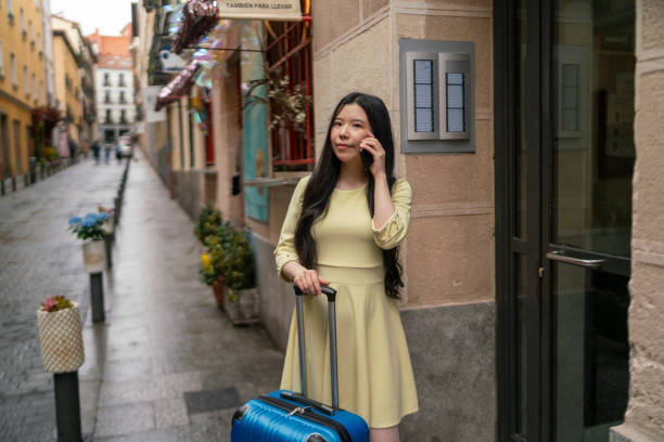 A tourist girl with her suitcase calling with her mobile phone in a tourist flat. stock photo