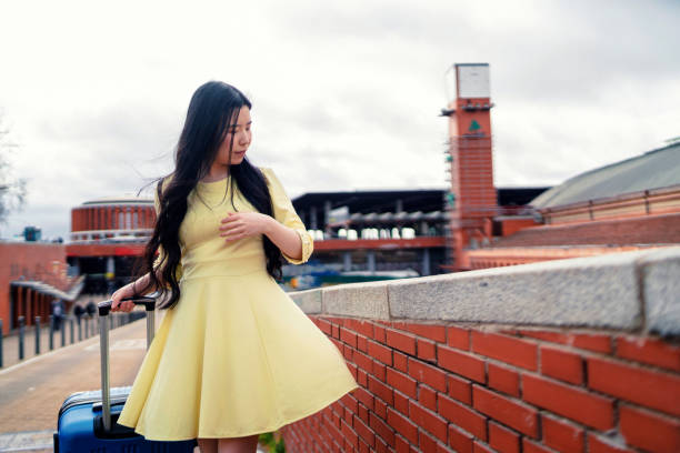 a girl with her blue suitcase and dressed in yellow at the station stock photo