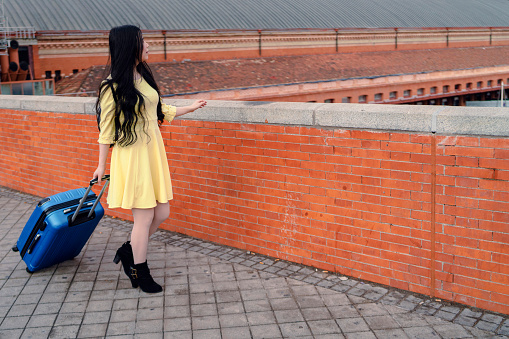 a girl with her blue suitcase and dressed in yellow at the station
