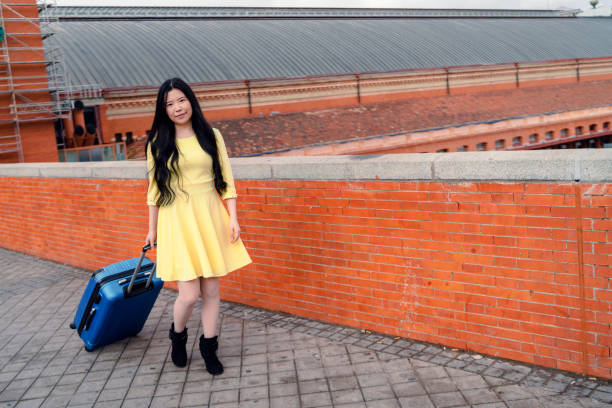 a girl with her blue suitcase and dressed in yellow at the station stock photo