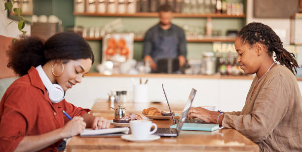 Students writing, studying on laptop in cafe for elearning, university education or working remote. Black women, friends and college research in coffee shop together for collaboration or teamwork