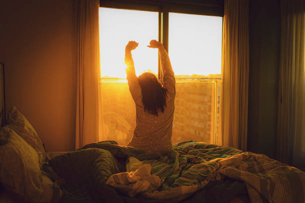 istock Woman looking through window stretching arms in the morning 1474811821