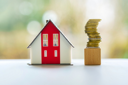 Miniature House Model with a Tower of Stacked Coins Concept for: Building, Loan Value, Renting or Buying Real Estate