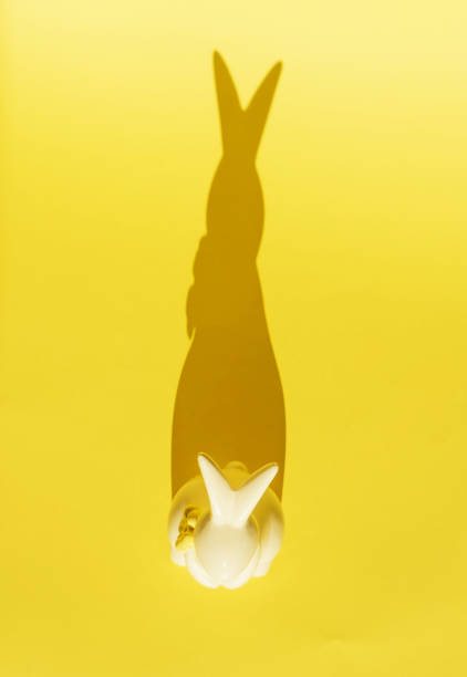 Creative photo. Ceramic Easter bunny on a yellow monochrome background, the shadow of a rabbit silhouette, a modern concept and decoration for Easter. Space for copying