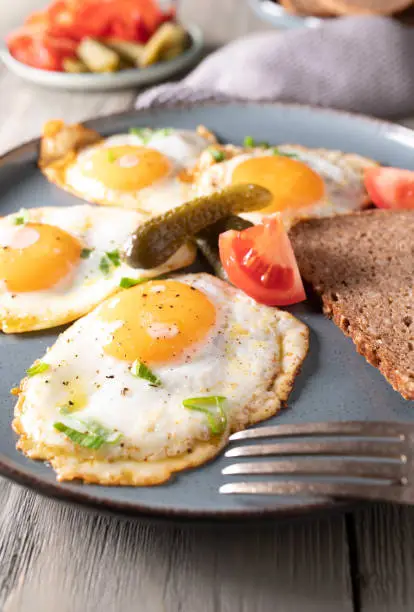 Traditional german breakfast, lunch or dinner with fried eggs, sunny side up. Served with pickles, tomatoes and bread on a plate. Closeup and front view