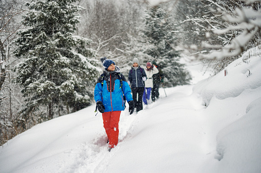 Mother and three kids are hiking in European Alps on a winter day. Family is walking on a path in the snow.\nSnowy overcast winter day.\nShot with Canon R5