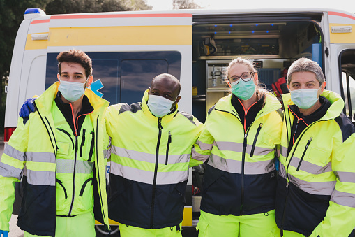 4 paramedics in front of an ambulance looking at camera and ready for emergency rescue services