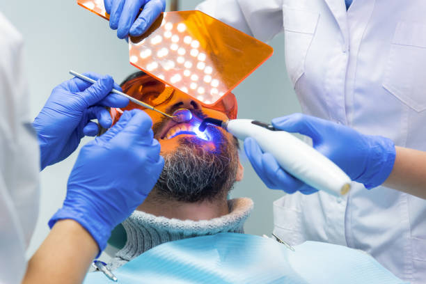 Two stomatologists at work. Two stomatologists at work. Dentist is using UV light. Qualified specialists and newest equipment. dental light stock pictures, royalty-free photos & images