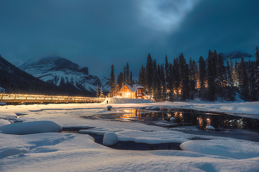 Beautiful scenery of Frozen Emerald Lake with wooden lodge glowing in snowfall on winter at the night in Yoho national park, Alberta, Canada